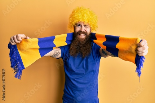 Redhead man with long beard football hooligan cheering game wearing funny wig winking looking at the camera with sexy expression, cheerful and happy face. photo