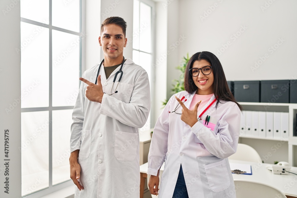 Young doctors wearing uniform and stethoscope at the clinic smiling cheerful pointing with hand and finger up to the side Young doctors wearing uniform and stethoscope at the clinic smiling cheerful pointing with hand and finger up to the side