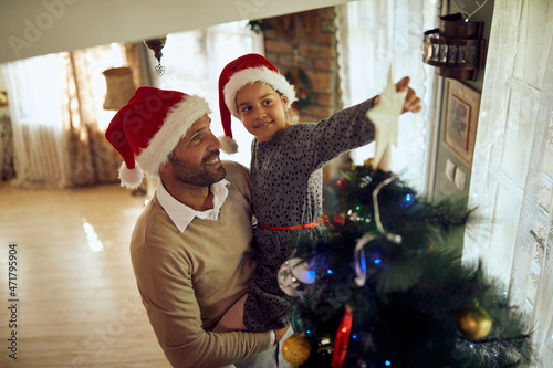 Happy little girl decorates Christmas tree with her father and putts star on top it.