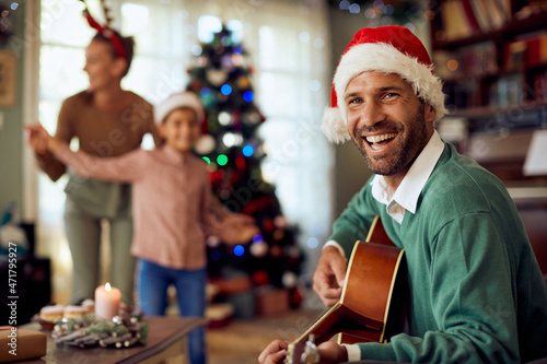 Happy father plays acoustic guitar to his family while celebrating Christmas at home.
