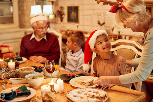 Happy little girl talks to her grandmother while she is serving her apple pie during family lunch on Christmas.