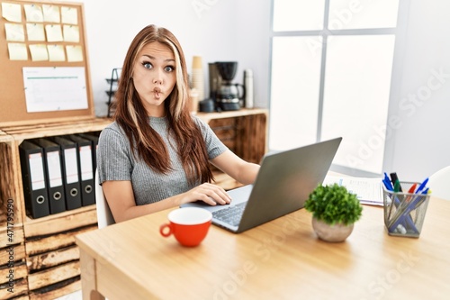 Young brunette woman working at the office with laptop making fish face with lips, crazy and comical gesture. funny expression.