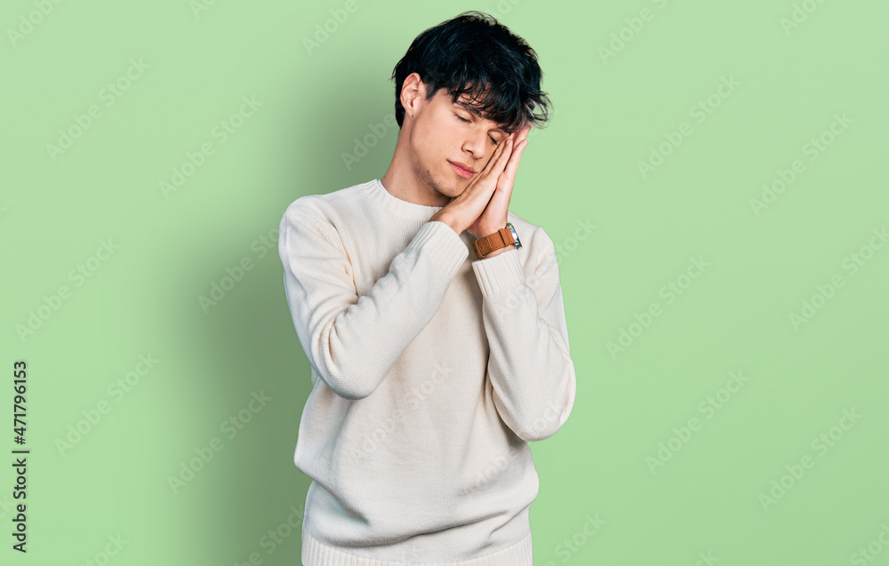 Handsome hipster young man wearing casual winter sweater sleeping tired dreaming and posing with hands together while smiling with closed eyes. Handsome hipster young man wearing casual winter sweater sleeping tired dreaming and posing with hands together while smiling with closed eyes.