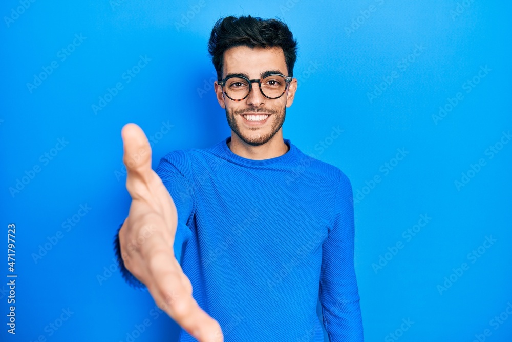 Young hispanic man wearing casual clothes and glasses smiling friendly offering handshake as greeting and welcoming. successful business. Young hispanic man wearing casual clothes and glasses smiling friendly offering handshake as greeting and welcoming. successful business.