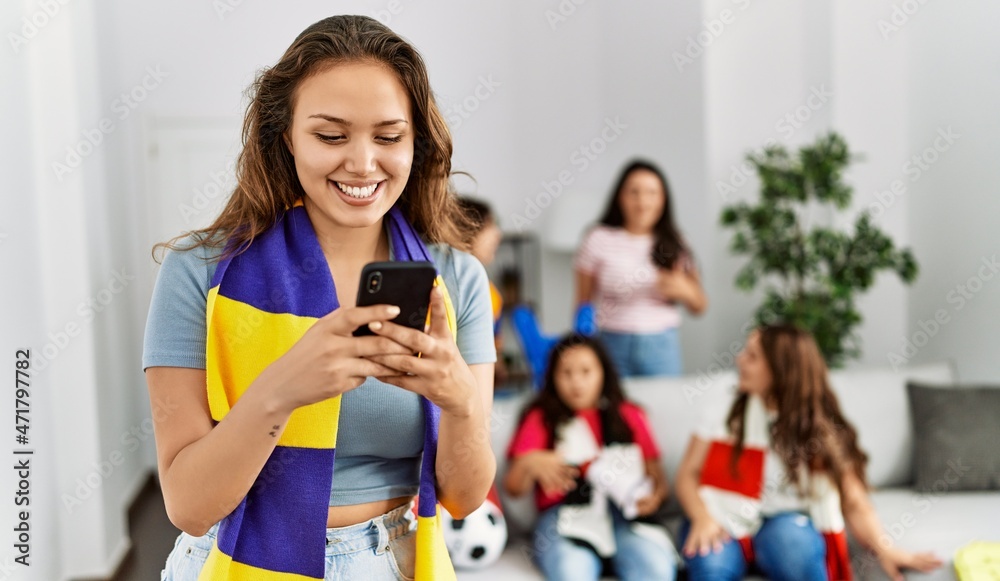 Obraz premium Group of young women watching and supporting soccer match. Hispanic woman smiling happy and using smartphone at home.