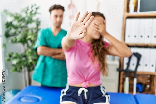 Young hispanic woman at physiotherapist appointment covering eyes with hands and doing stop gesture with sad and fear expression. embarrassed and negative concept.