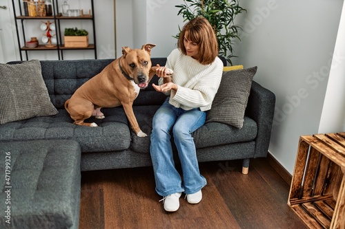 Young caucasian woman feeding dog sitting on sofa at home