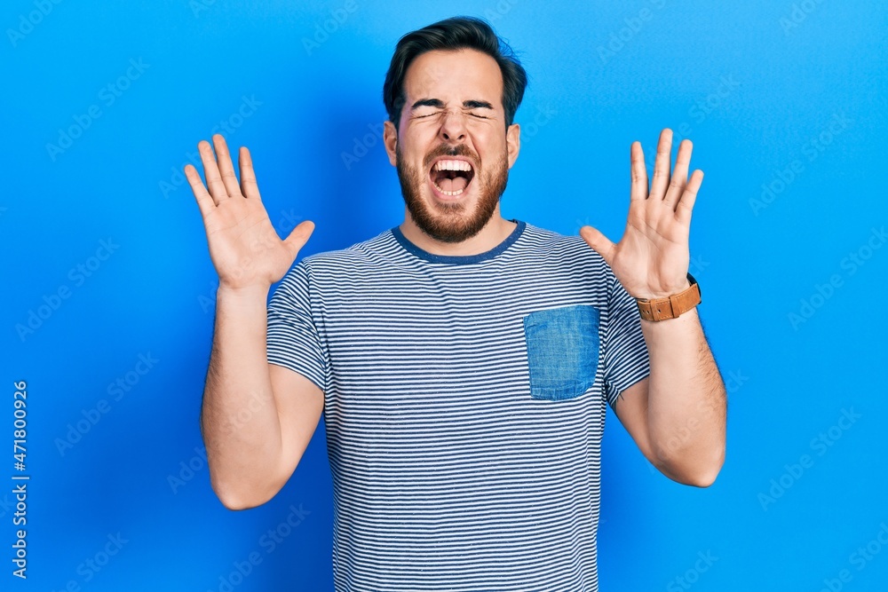 Fototapeta premium Handsome caucasian man with beard wearing casual striped t shirt celebrating mad and crazy for success with arms raised and closed eyes screaming excited. winner concept