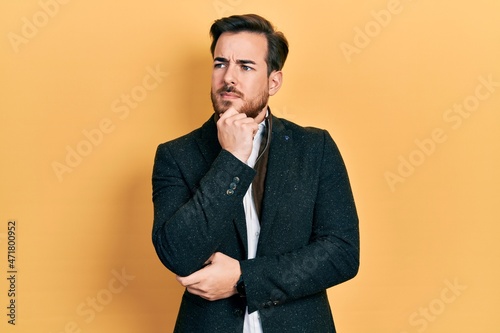 Handsome caucasian man with beard wearing elegant business jacket serious face thinking about question with hand on chin, thoughtful about confusing idea