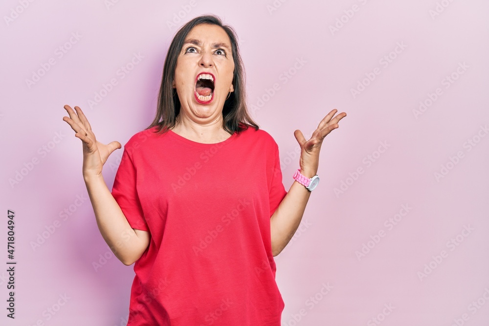Middle age hispanic woman wearing casual clothes crazy and mad shouting and yelling with aggressive expression and arms raised. frustration concept.