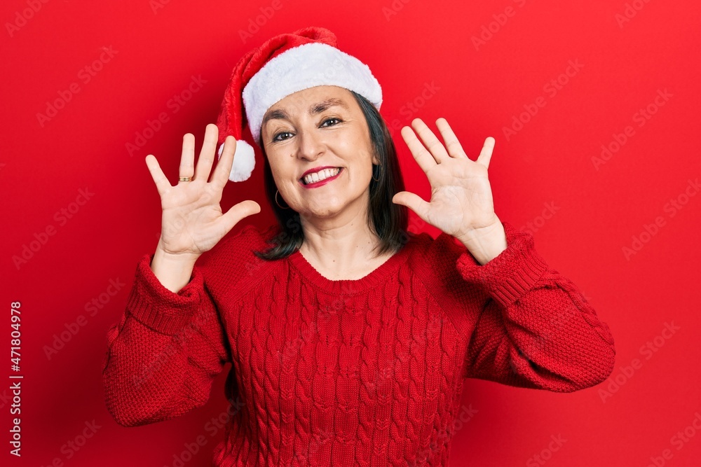 Middle age hispanic woman wearing christmas hat showing and pointing up with fingers number ten while smiling confident and happy. Middle age hispanic woman wearing christmas hat showing and pointing up with fingers number ten while smiling confident and happy.