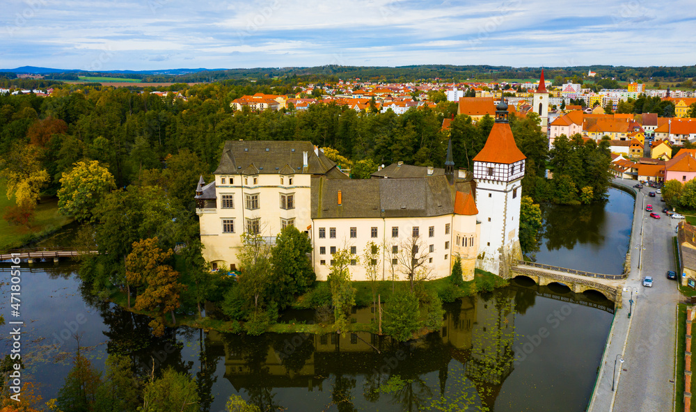 Obraz premium Aerial view of medieval Blatna water castle surrounded parks and lakes on background with cityscape on autumn day, South Bohemian Region, Czech Republic..