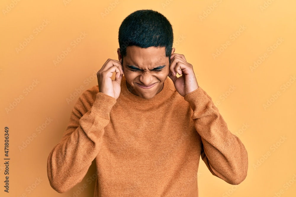 Young handsome hispanic man wearing casual winter sweater covering ears with fingers with annoyed expression for the noise of loud music. deaf concept.