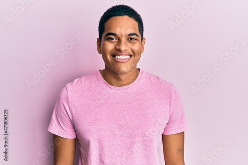 Young handsome hispanic man wearing casual pink t shirt with a happy and cool smile on face. lucky person.