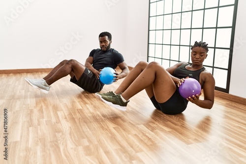 Young african american sporty couple doing abs exercise using ball at sport center.