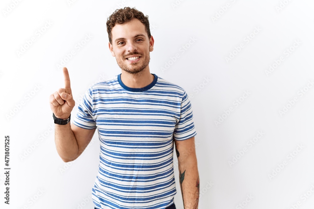 Handsome young man standing over isolated background showing and pointing up with finger number one while smiling confident and happy. Handsome young man standing over isolated background showing and pointing up with finger number one while smiling confident and happy.
