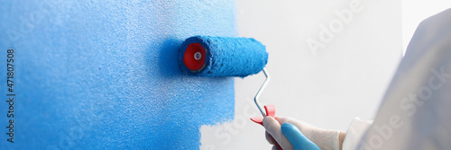 Repairman painting white wall in apartment blue using roller closeup photo