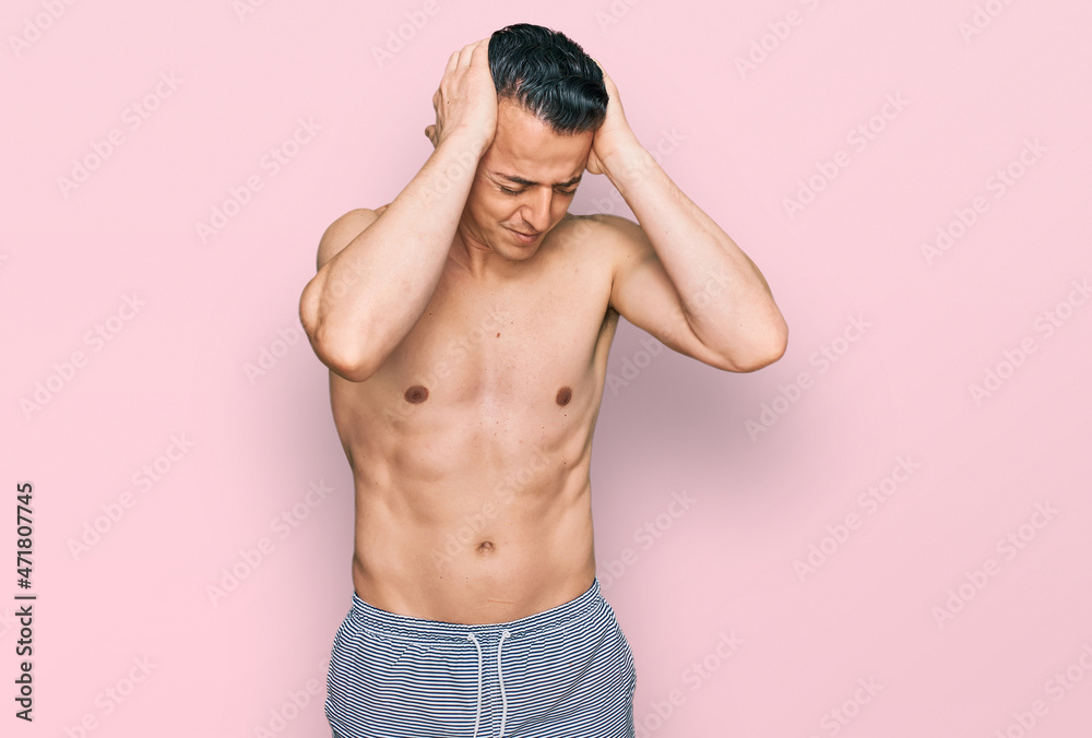 Handsome young man wearing swimwear shirtless suffering from headache desperate and stressed because pain and migraine. hands on head.