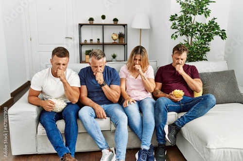 Group of middle age people sitting on the sofa at home feeling unwell and coughing as symptom for cold or bronchitis. health care concept.