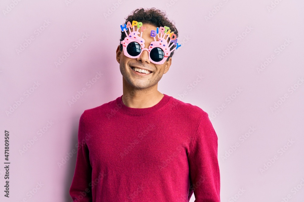 Handsome hispanic man wearing funny happy birthday glasses with a happy and cool smile on face. lucky person. Handsome hispanic man wearing funny happy birthday glasses with a happy and cool smile on face. lucky person.