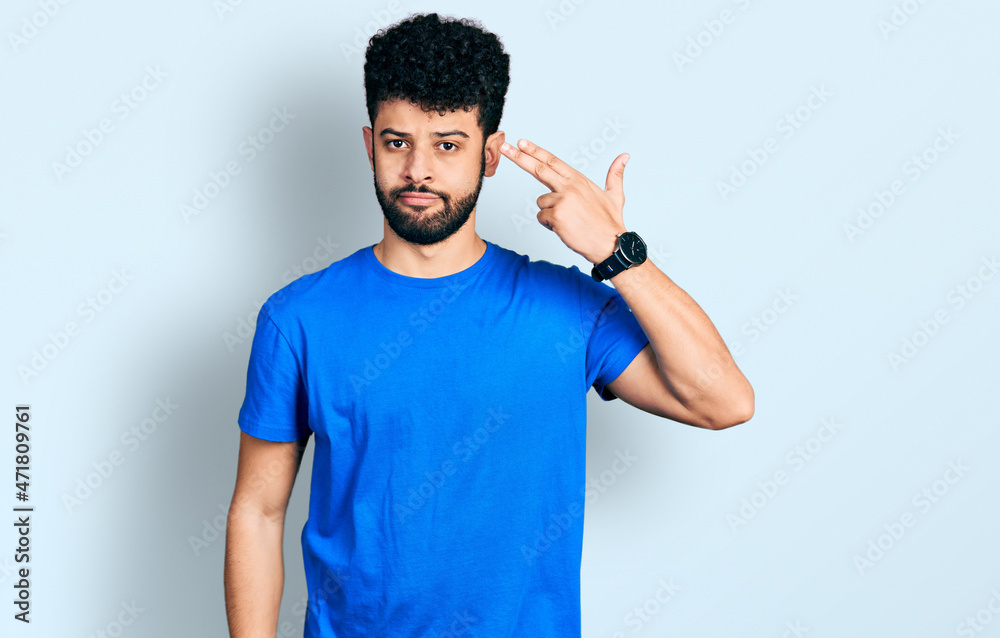 Young arab man with beard wearing casual blue t shirt shooting and killing oneself pointing hand and fingers to head like gun, suicide gesture. Young arab man with beard wearing casual blue t shirt shooting and killing oneself pointing hand and fingers to head like gun, suicide gesture.