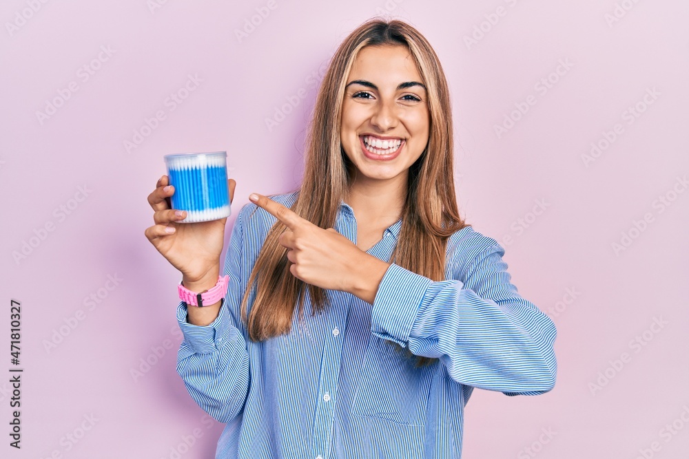 Beautiful hispanic woman holding earwax cotton removers smiling happy pointing with hand and finger