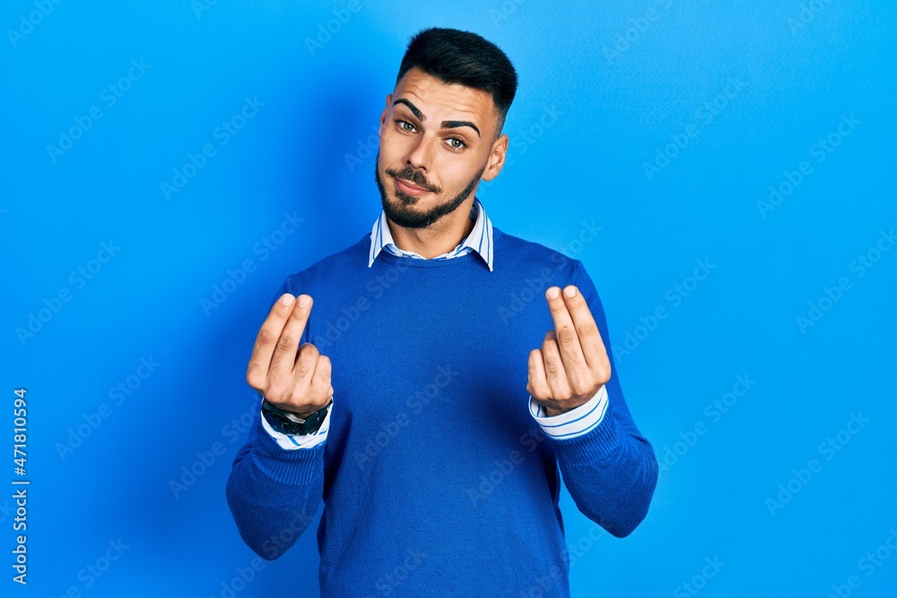 Young hispanic man with beard wearing casual blue sweater doing money gesture with hands, asking for salary payment, millionaire business Young hispanic man with beard wearing casual blue sweater doing money gesture with hands, asking for salary payment, millionaire business
