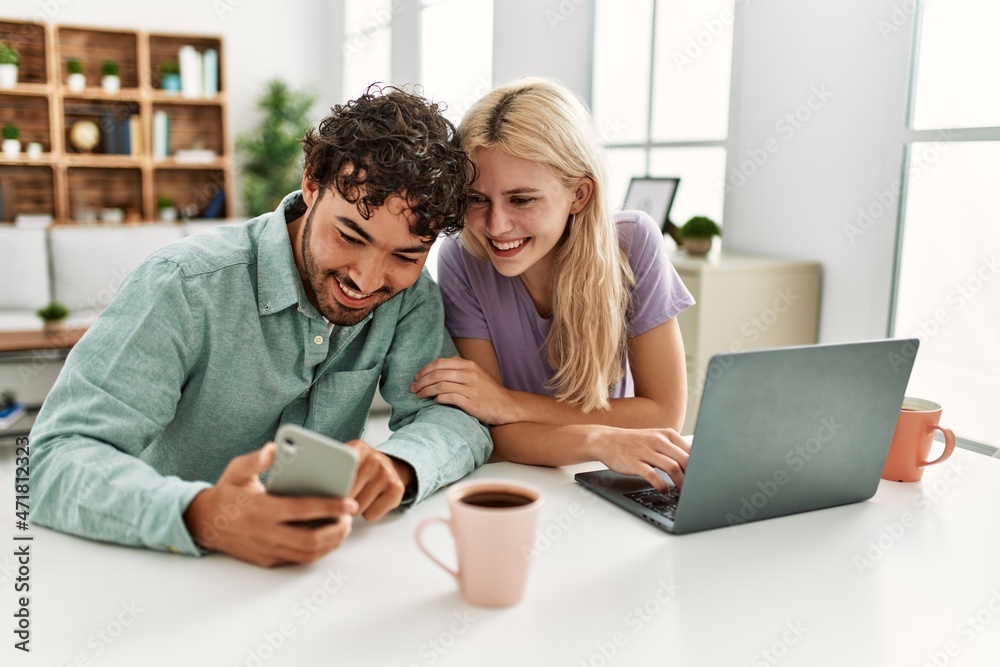 Young couple using laptop and smartphone drinking coffee at home. Young couple using laptop and smartphone drinking coffee at home.