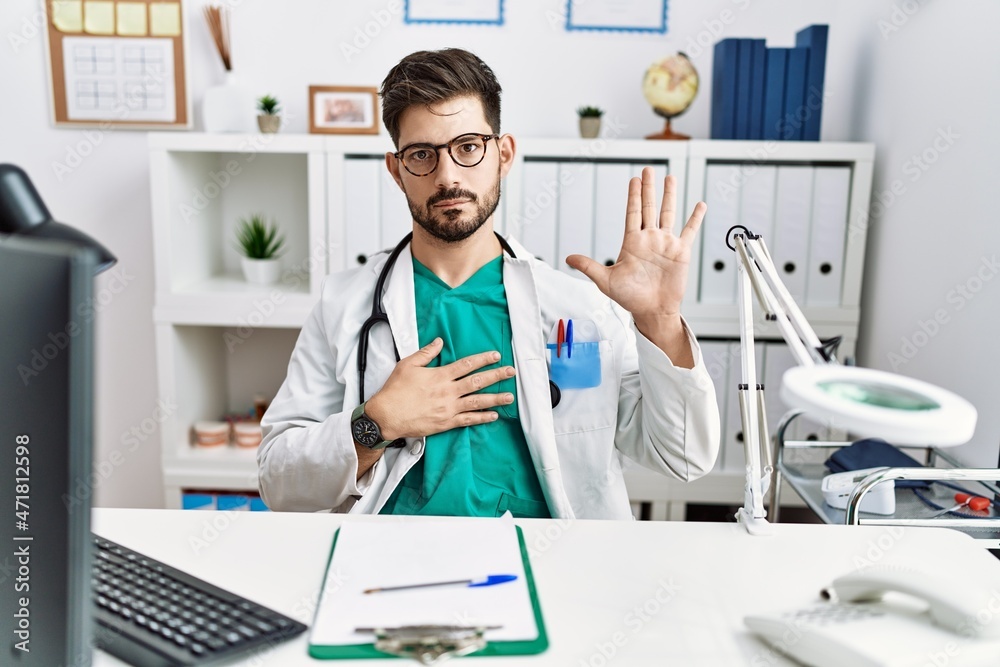 Young man with beard wearing doctor uniform and stethoscope at the clinic swearing with hand on chest and open palm, making a loyalty promise oath Young man with beard wearing doctor uniform and stethoscope at the clinic swearing with hand on chest and open palm, making a loyalty promise oath