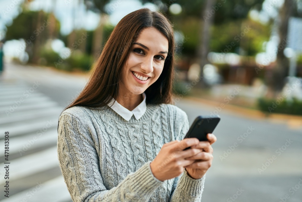 Young hispanic woman smiling happy using smartphone at the city.