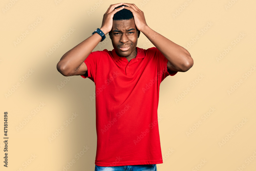 Young african american man wearing casual red t shirt suffering from headache desperate and stressed because pain and migraine. hands on head. Young african american man wearing casual red t shirt suffering from headache desperate and stressed because pain and migraine. hands on head.