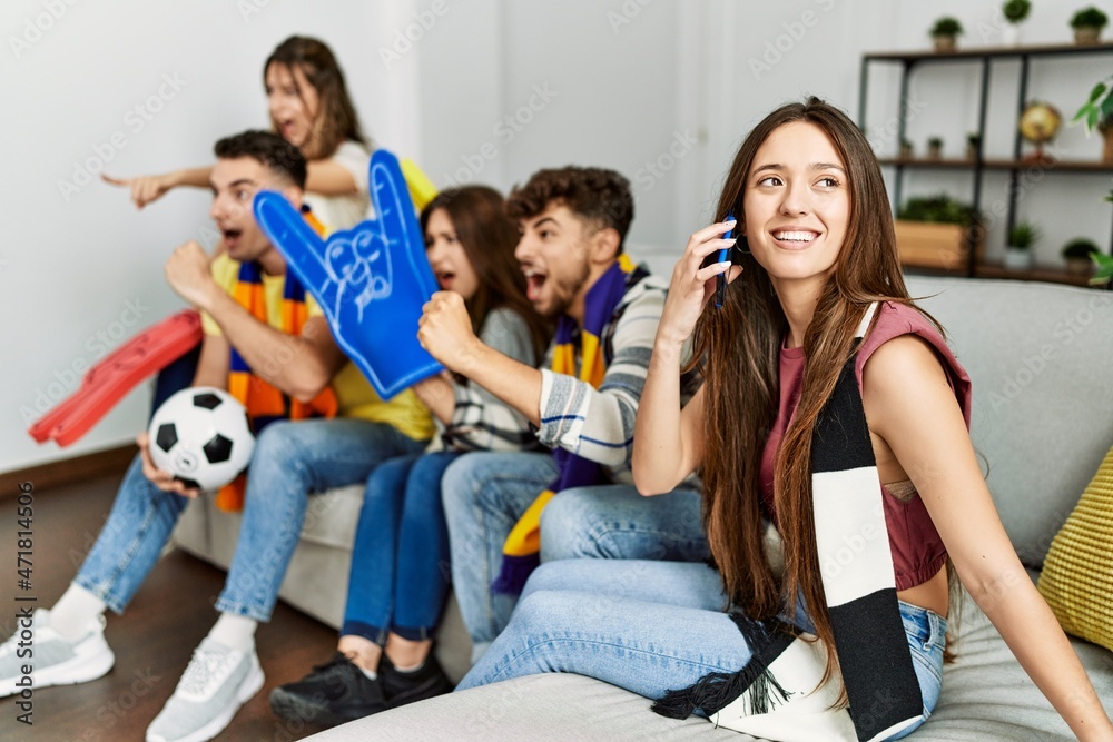 Obraz premium Group of young friends watching and supporting soccer match. Woman talking on the smartphone at home.