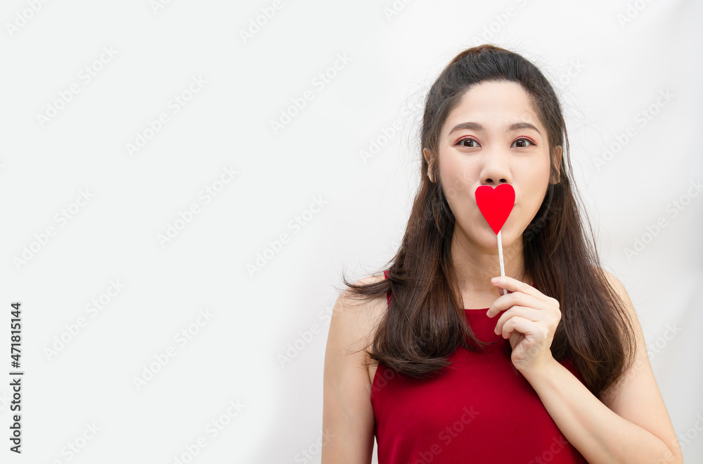 Asian beautiful woman with red theme are holding red heart shape paper stick covering her mouth with a smiling and happiness Asian beautiful woman with red theme are holding red heart shape paper stick covering her mouth with a smiling and happiness