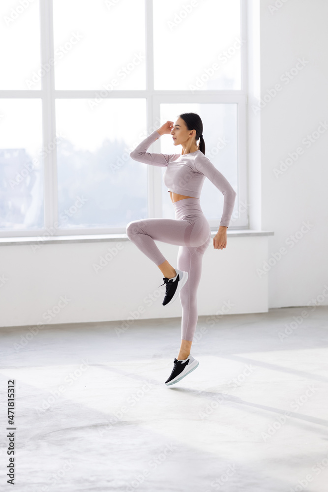 Full length portrait of a young fitness woman in sportswear posing and jumping at gym