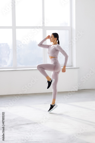 Full length portrait of a young fitness woman in sportswear posing and jumping at gym