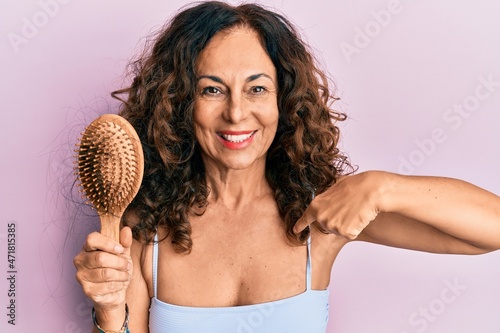 Middle age hispanic woman using comb pointing finger to one self smiling happy and proud