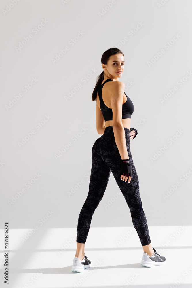 Rear view of fit fitness woman in leggings, turn head at camera with confident face expression, standing over white background Rear view of fit fitness woman in leggings, turn head at camera with confident face expression, standing over white background