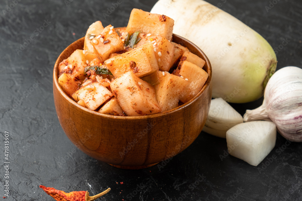 Fermented Korean daikon radish slices in a wooden bowl on a dark