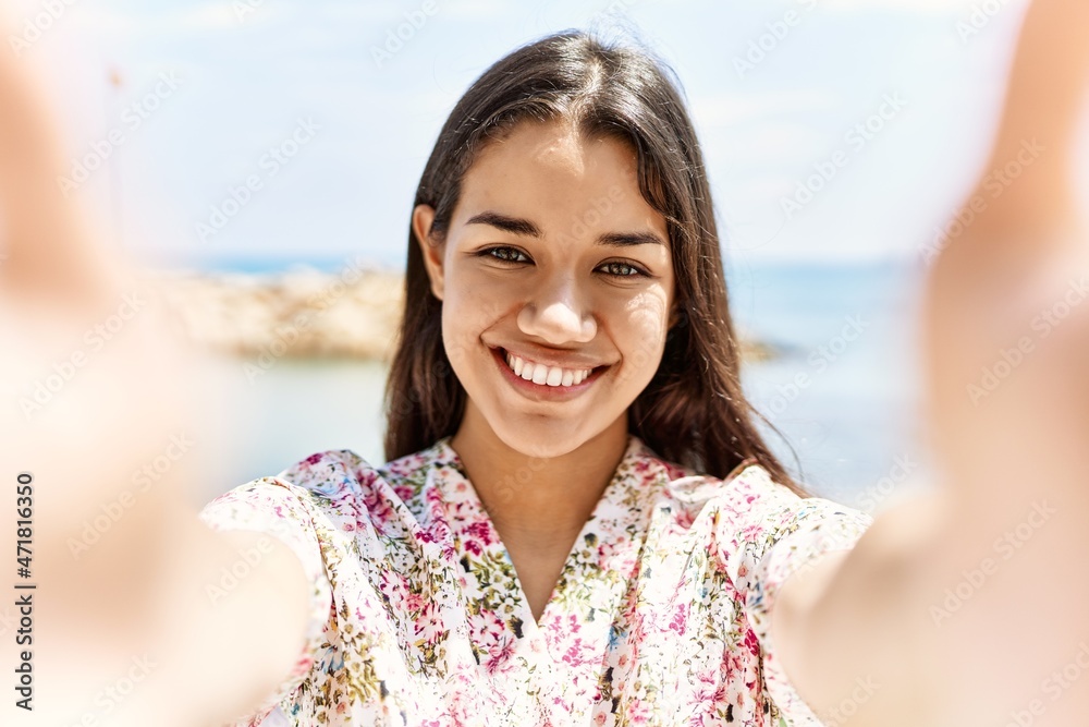 Young latin woman smiling confident make selfie by the camera at seaside