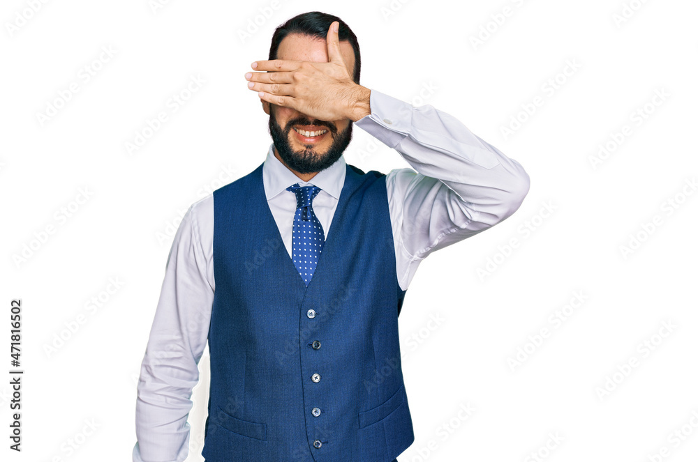 Young man with beard wearing business vest smiling and laughing with hand on face covering eyes for surprise. blind concept. Young man with beard wearing business vest smiling and laughing with hand on face covering eyes for surprise. blind concept.