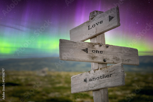 love one another text quote on wooden signpost outdoors in nature with northern lights above. photo