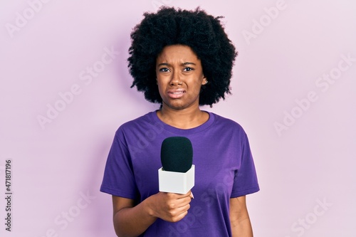 Young african american woman holding reporter microphone clueless and confused expression. doubt concept.