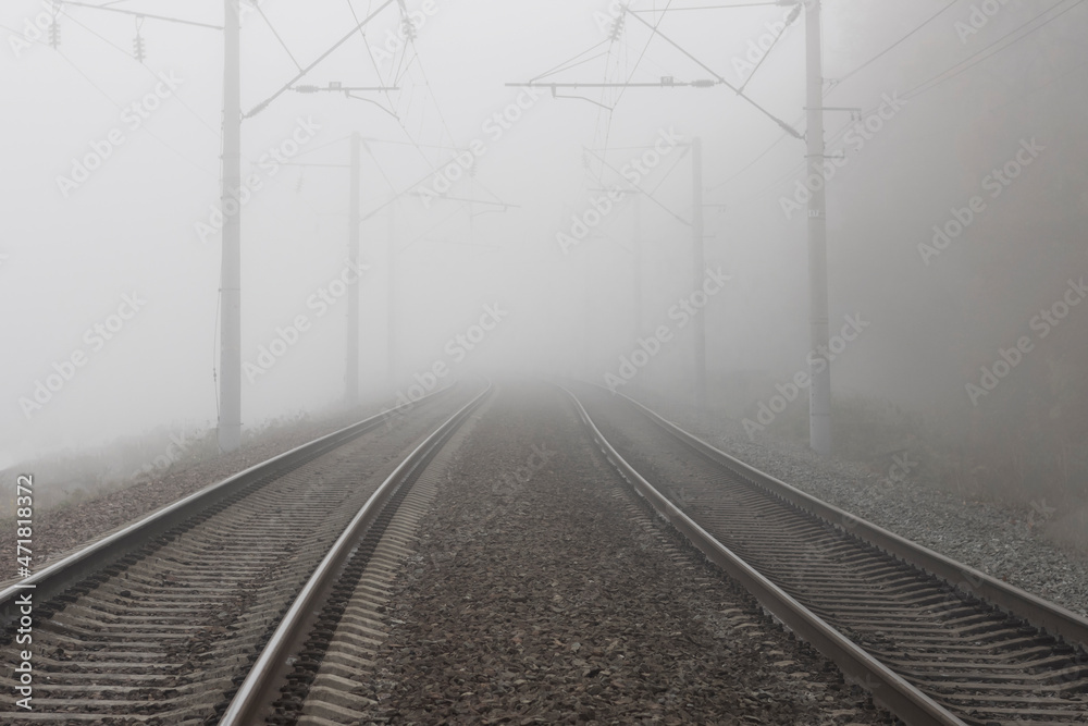 A railroad going into fog in the middle of an autumn landscape. Rails lost in the distance and disappearing into the fog.