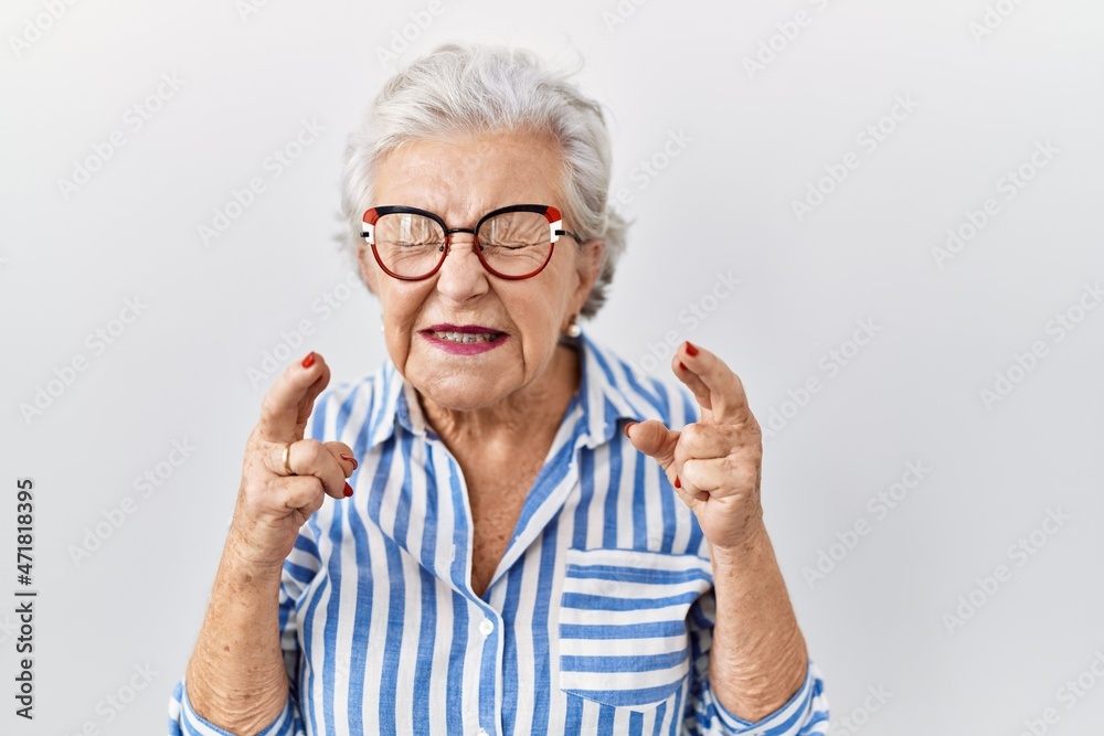 Senior woman with grey hair standing over white background gesturing finger crossed smiling with hope and eyes closed. luck and superstitious concept. Senior woman with grey hair standing over white background gesturing finger crossed smiling with hope and eyes closed. luck and superstitious concept.