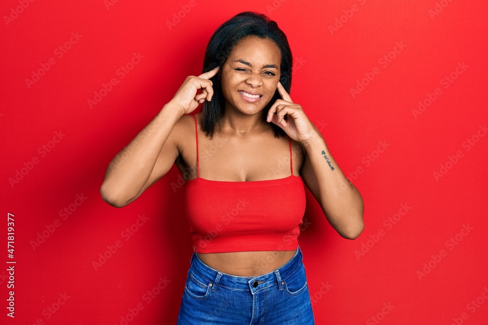 Young african american girl wearing casual style with sleeveless shirt covering ears with fingers with annoyed expression for the noise of loud music. deaf concept. Young african american girl wearing casual style with sleeveless shirt covering ears with fingers with annoyed expression for the noise of loud music. deaf concept.