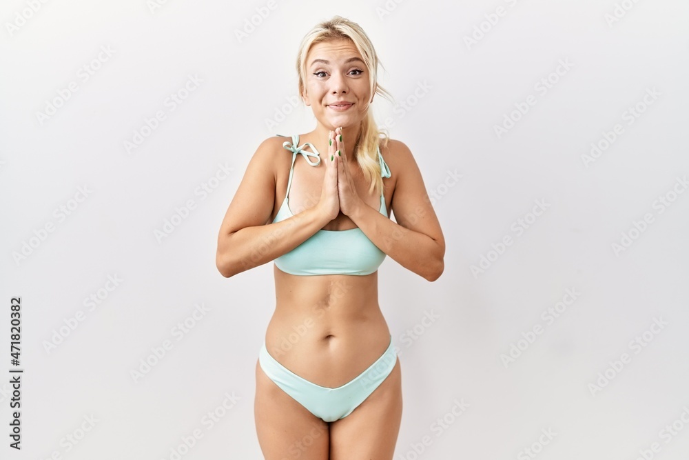 Young caucasian woman wearing bikini over isolated background praying with hands together asking for forgiveness smiling confident. Young caucasian woman wearing bikini over isolated background praying with hands together asking for forgiveness smiling confident.