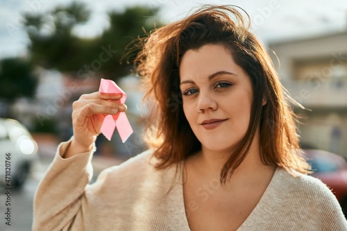 Young irish plus size girl smiling happy holding pink cancer ribbon at the city.