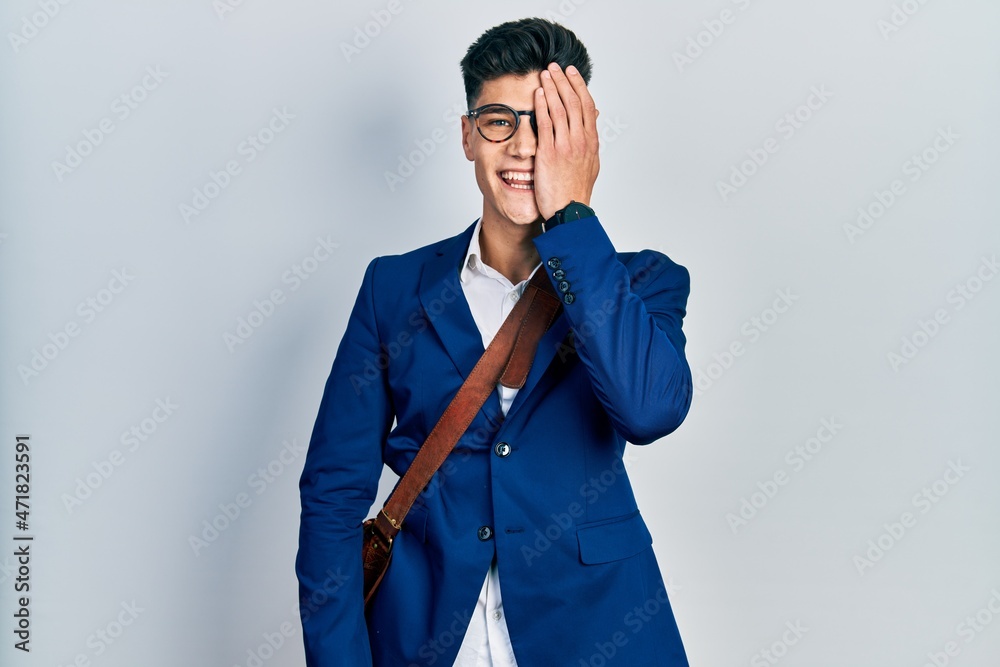 Young hispanic man wearing business clothes covering one eye with hand, confident smile on face and surprise emotion. Young hispanic man wearing business clothes covering one eye with hand, confident smile on face and surprise emotion.