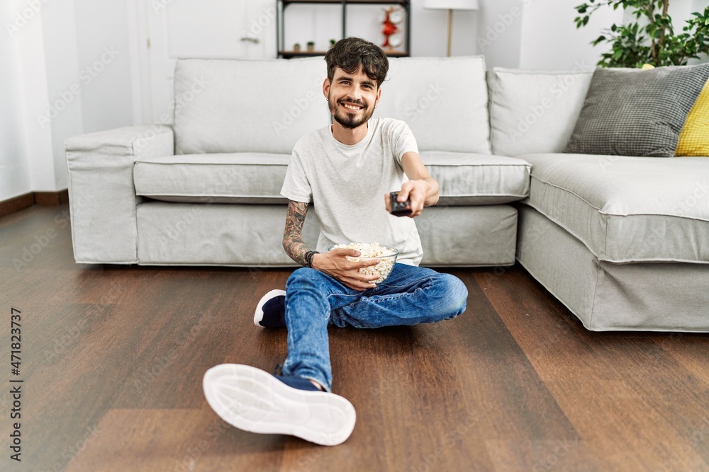 Young hispanic man watching movie sitting on the floor at home.