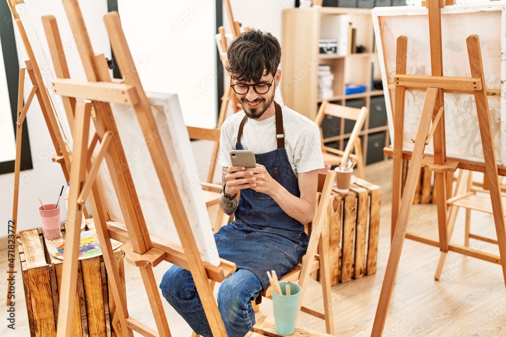 Young hispanic artist man using smartphone drawing at art studio.